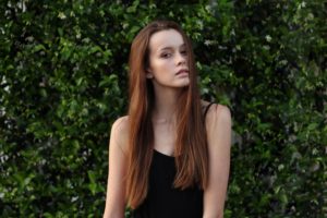 young white woman with long red hair, bare arms, greenery in back